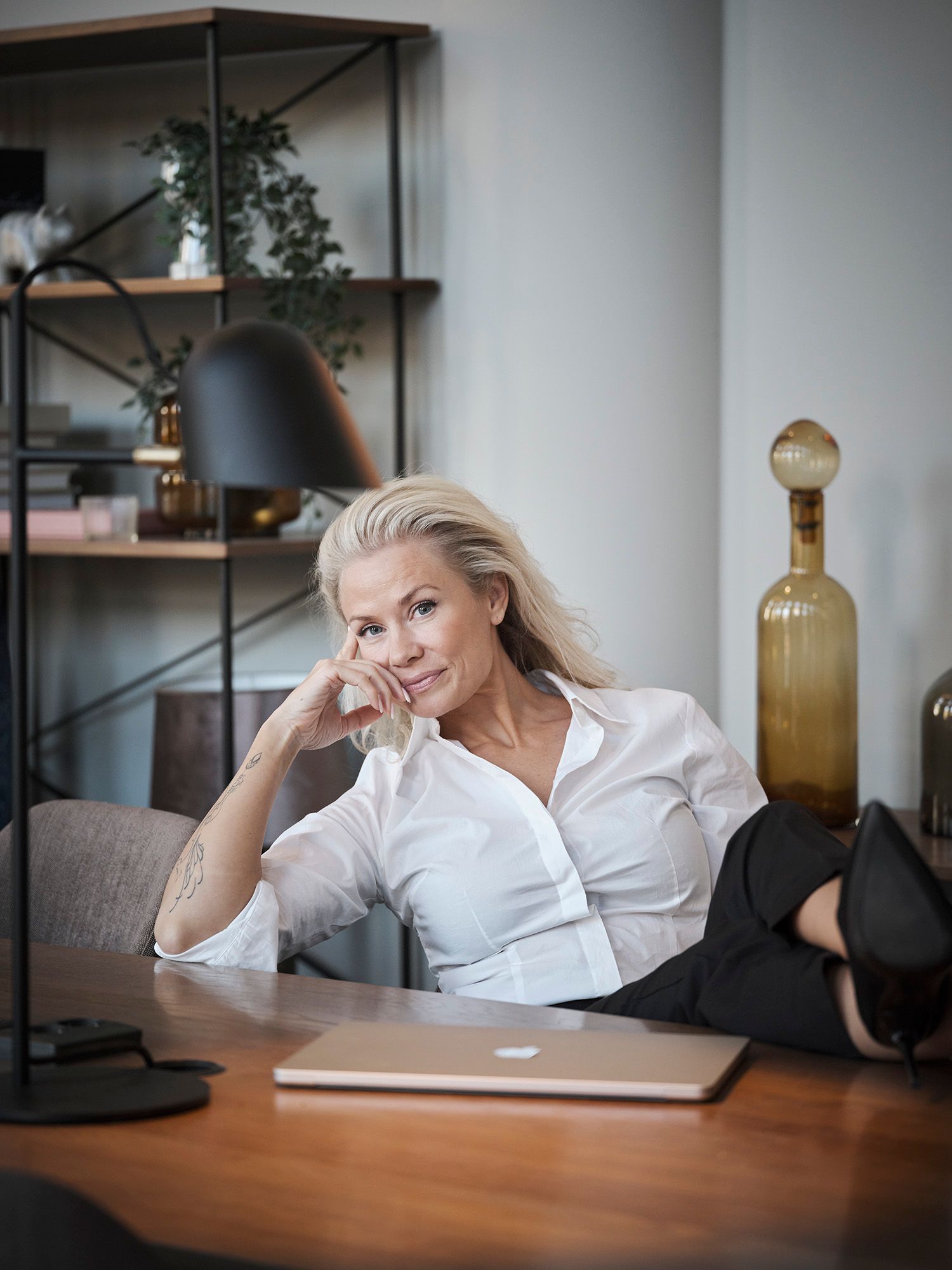 Blonde woman in white shirt sitting at a desk with a laptop in a stylish modern office setting.