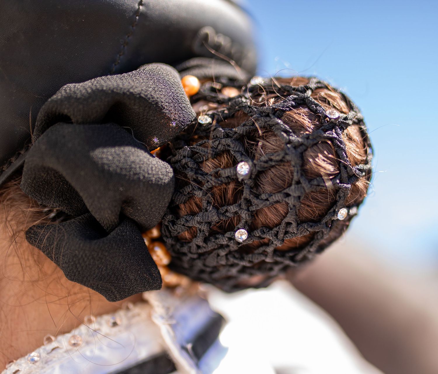 Close-up of a gloved hand holding a decorative black hair net with rhinestones for equestrian use.