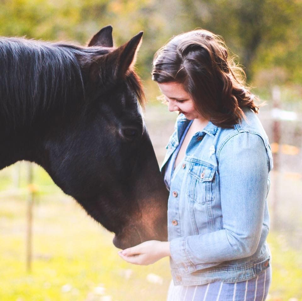 A girl smiles and pets her horse's nose.