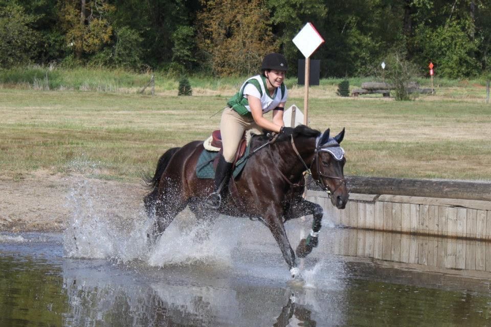 Horse runs through splashing water while its rider smiles.
