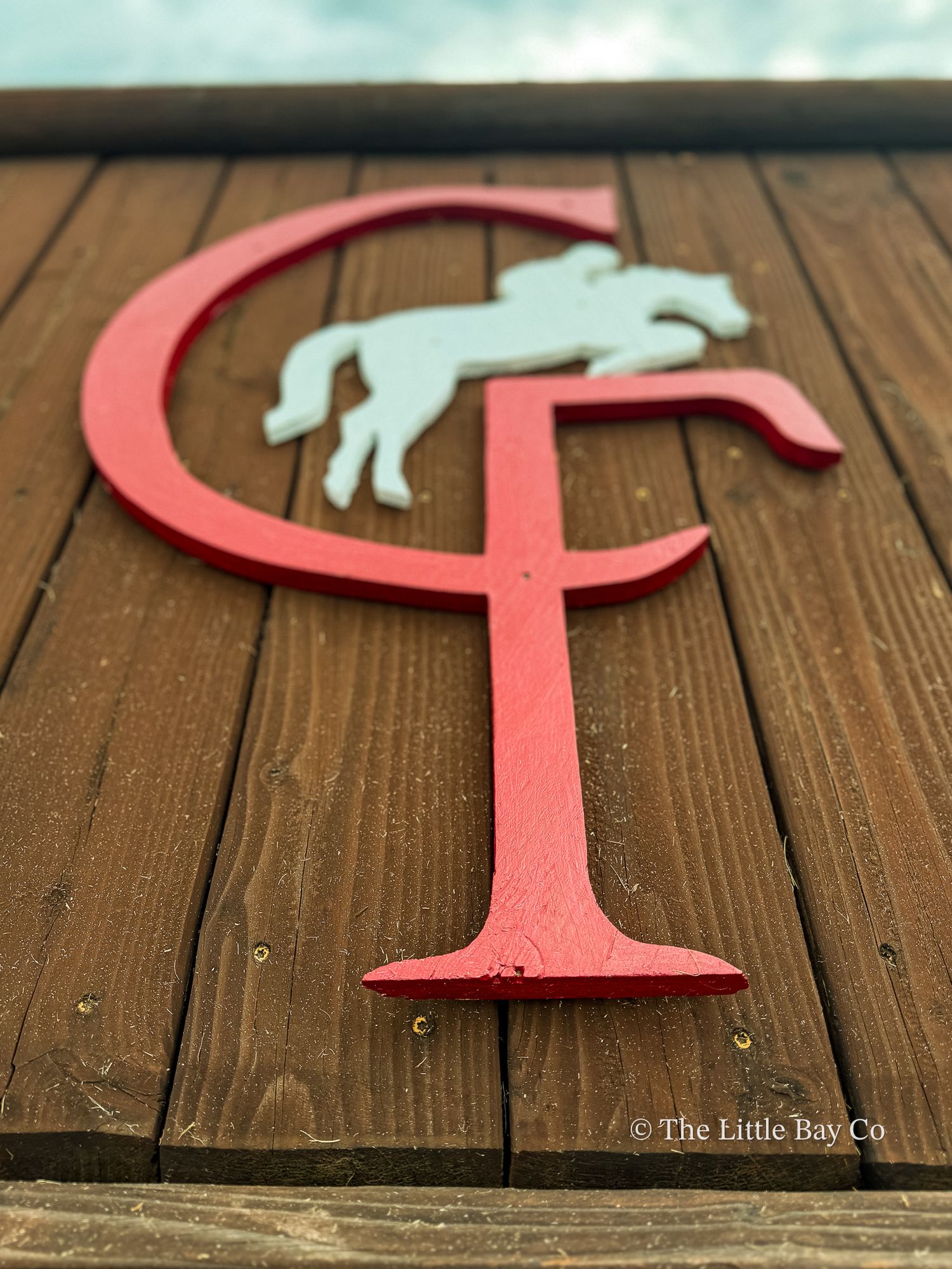 Red CF monogram logo with white jumping horse silhouette mounted on wooden wall, equestrian farm sign.