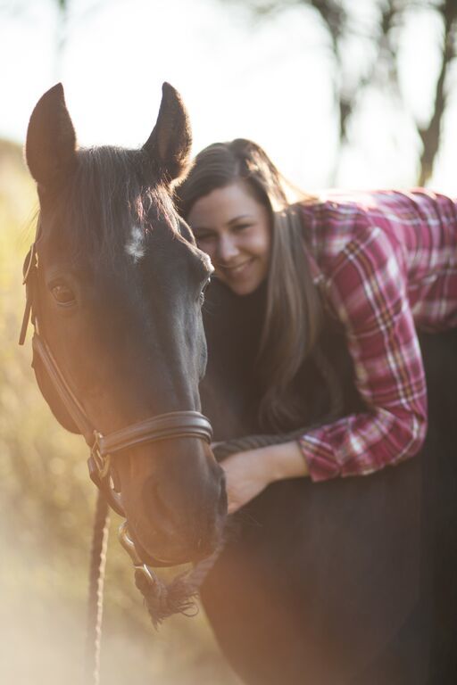 A girl lays on her horse's back, giving him a hug and smiling for the camera.
