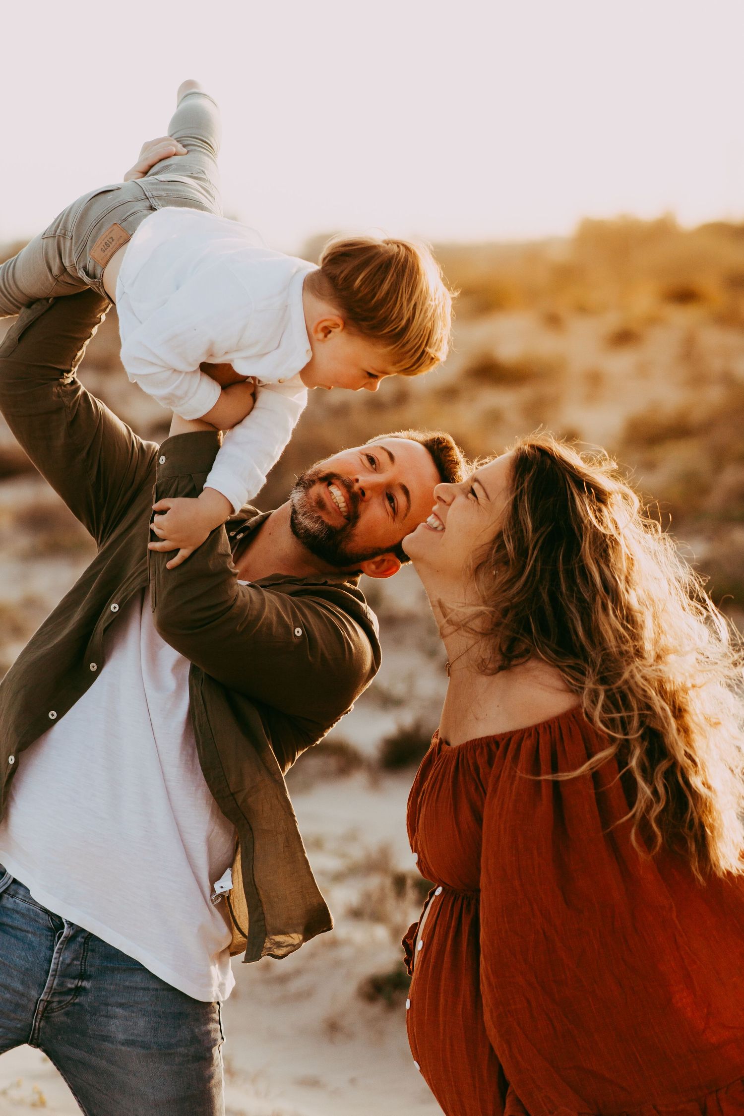 Padres jugando con su hijo durante una sesión de fotografía familiar en la playa.