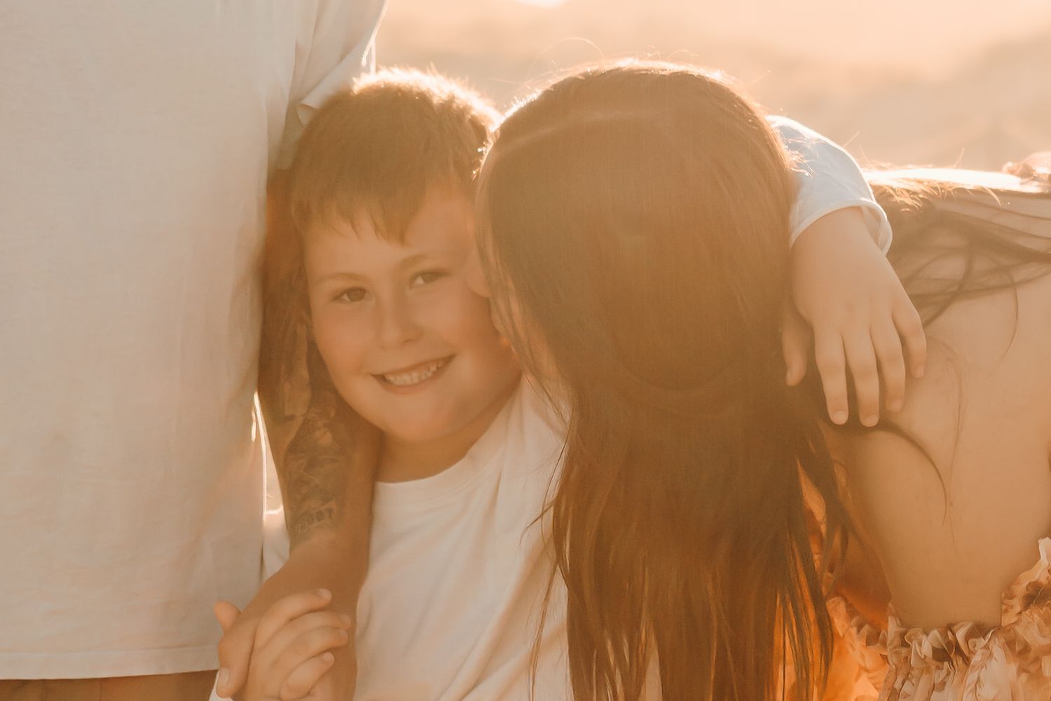 Madre abrazando a su hija durante una sesión de fotos familiar al atardecer en la playa de Girona.