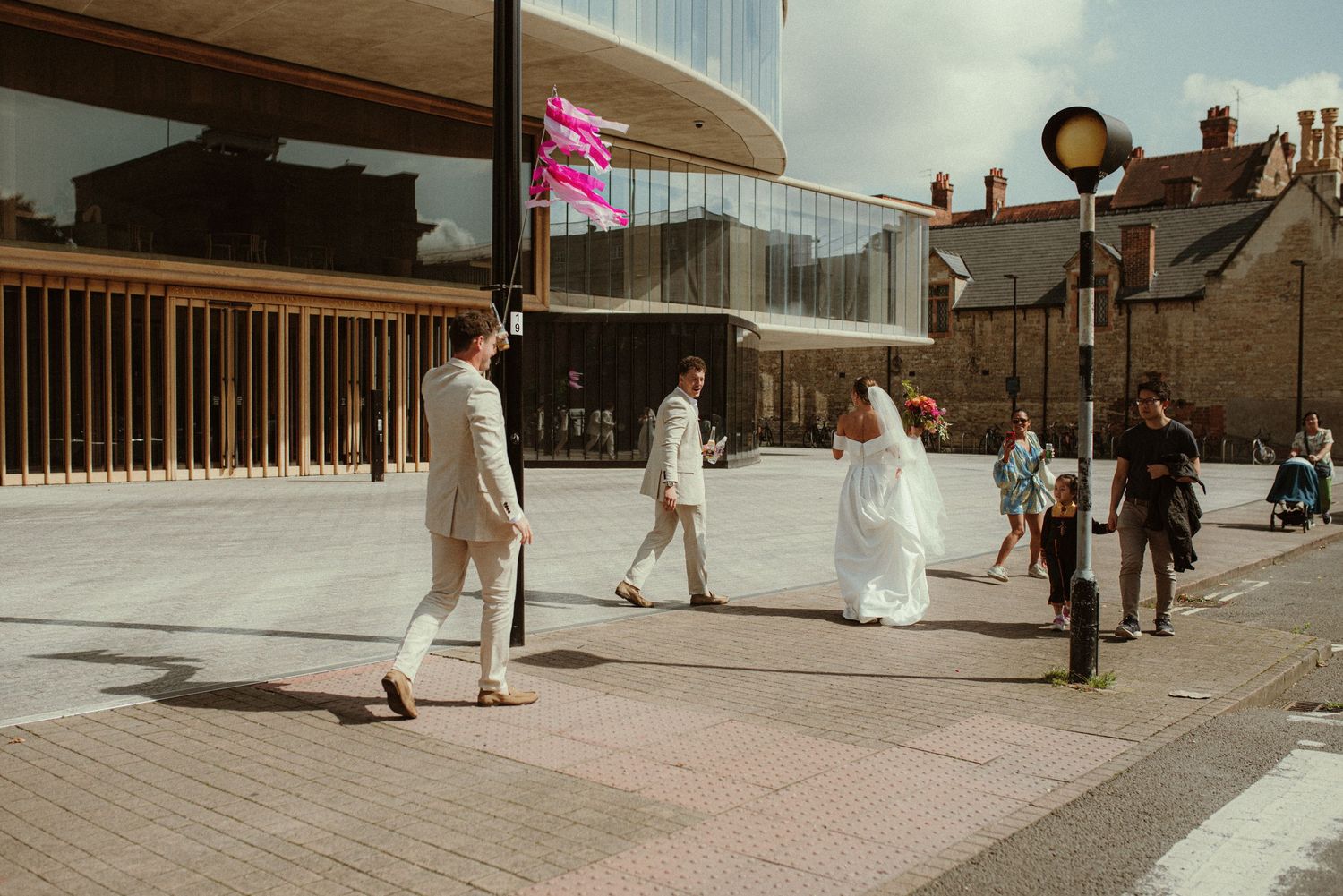People walking outside a modern building with curved architecture on a sunny day.