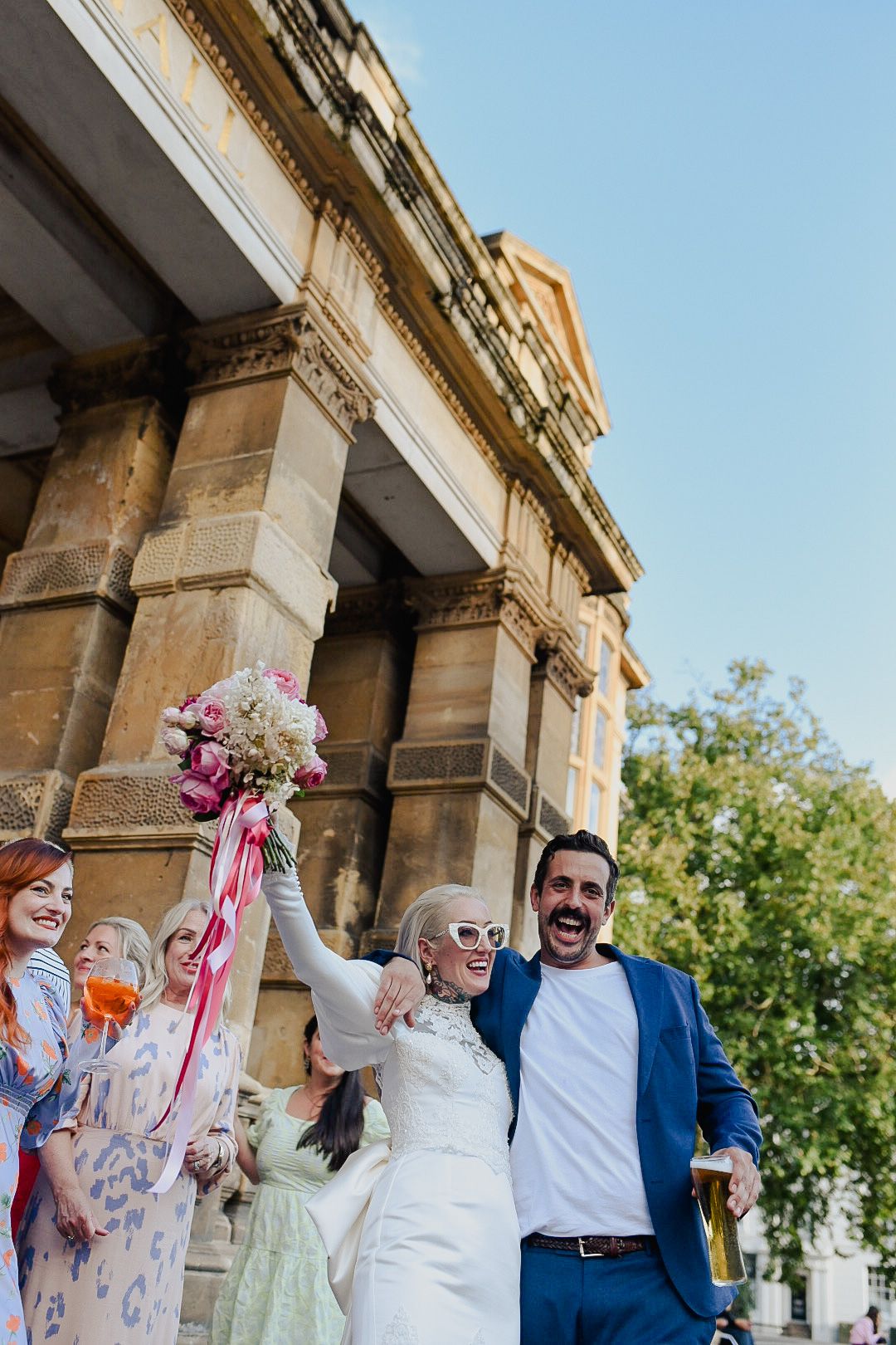 Newlyweds celebrating with guests outside historic stone building as bride holds pink floral bouquet.