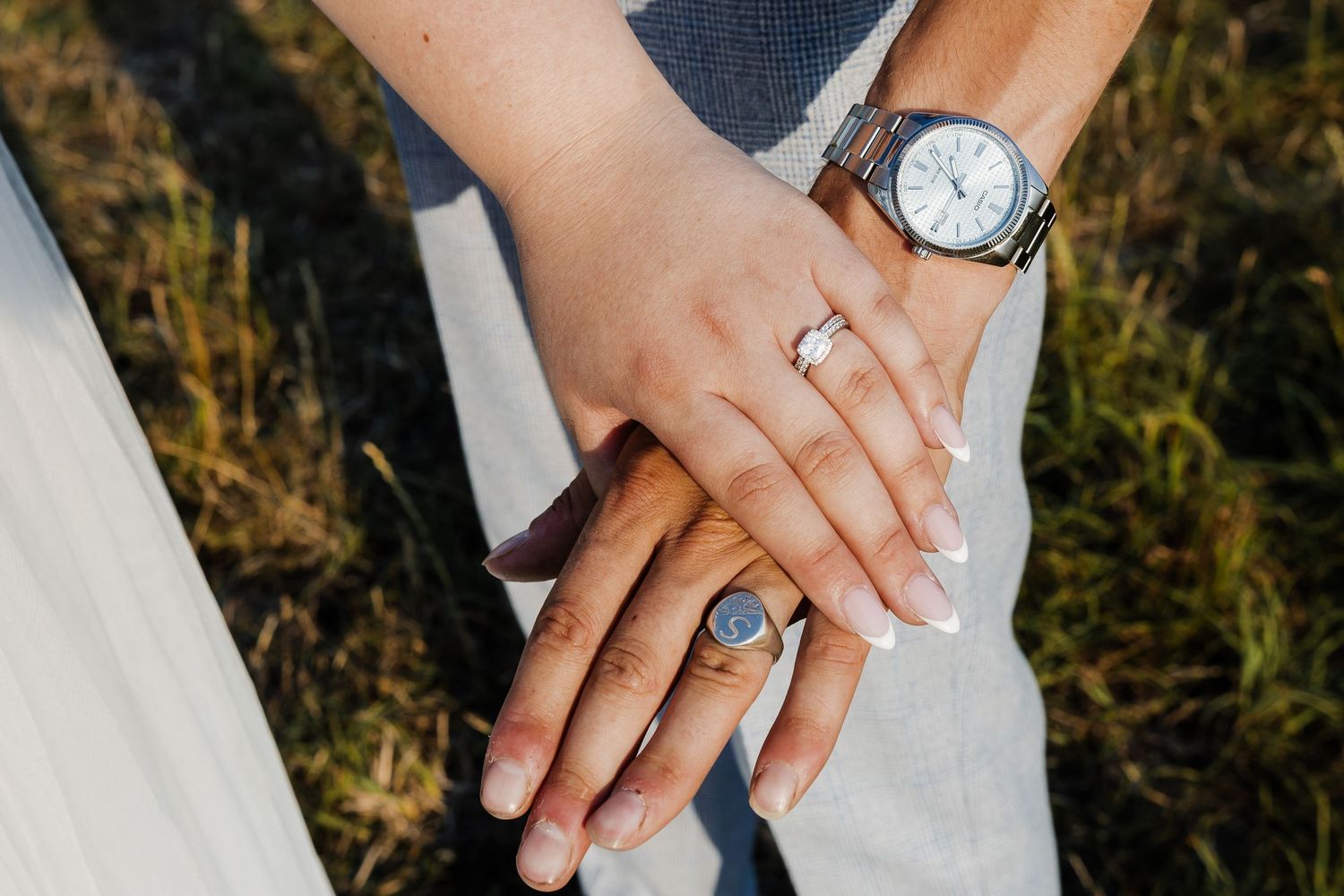 Wedding couple holds hands showing off rings against a blurred natural background outdoors.
