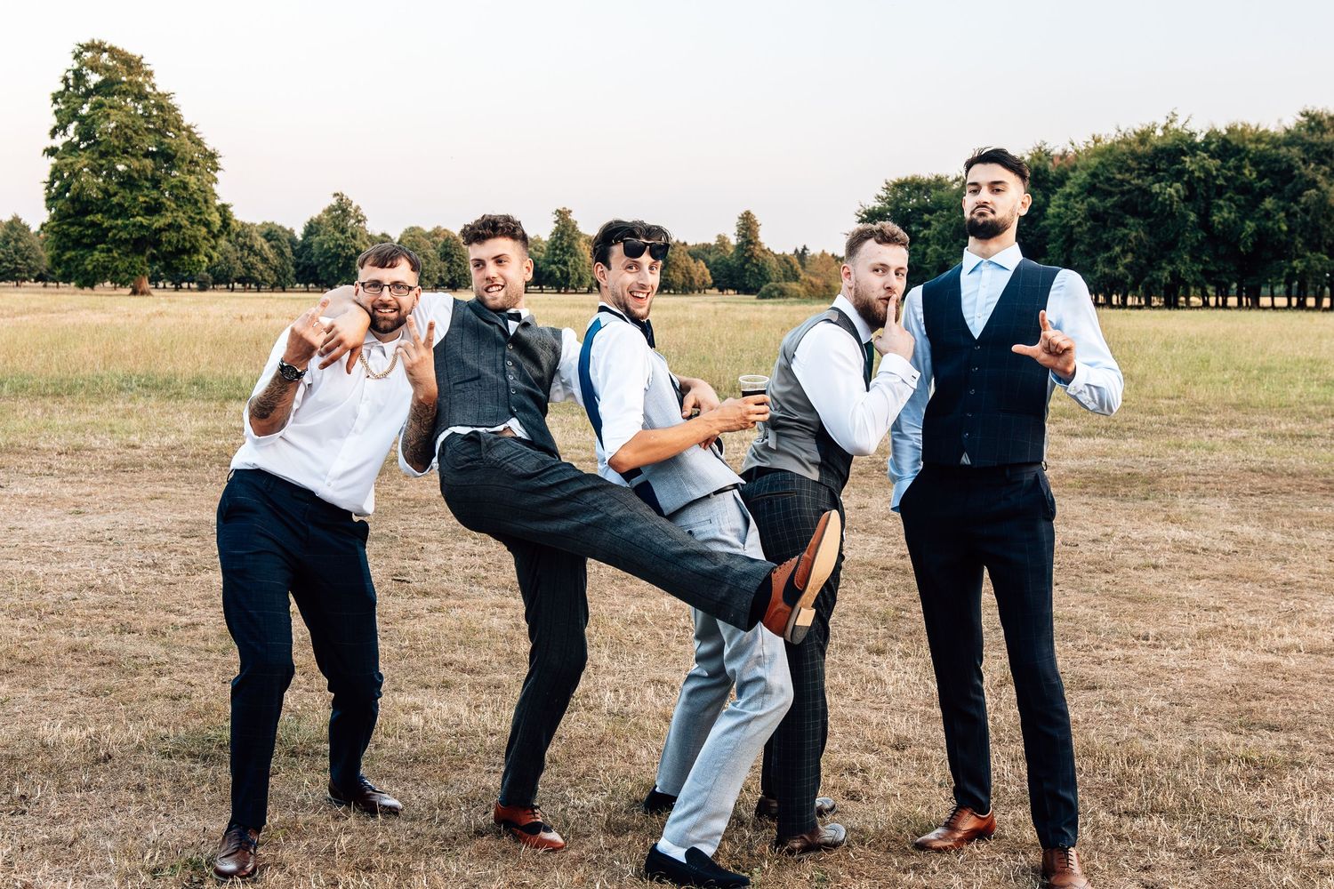 Wedding party poses playfully in a grassy field during summer celebration.