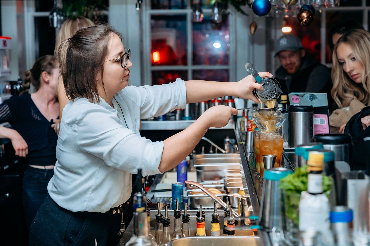 Professional bartender pouring colorful cocktails at an upscale bar during a busy evening service.