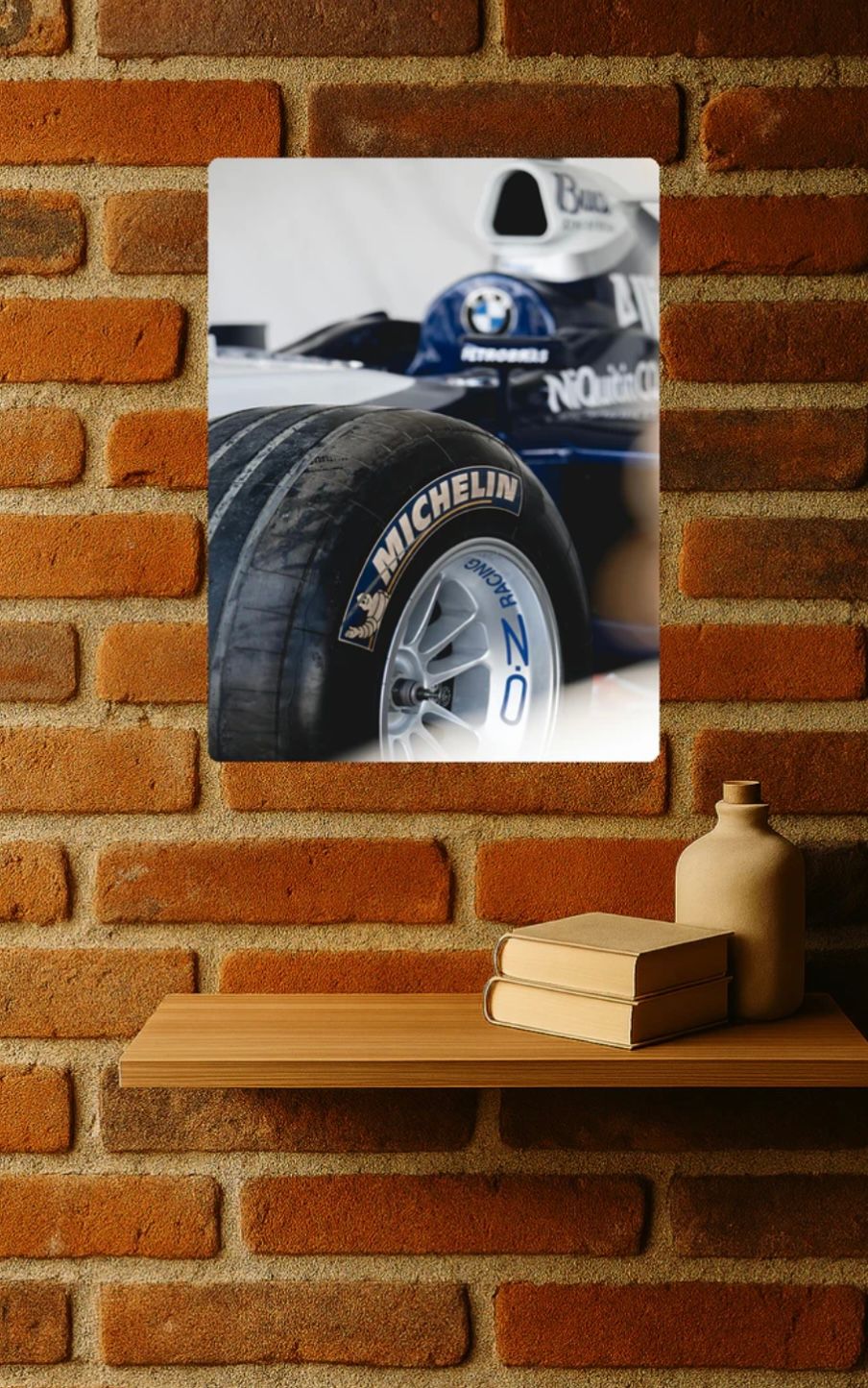 A framed Formula 1 racing car wheel detail photo showing Michelin tires mounted on a brick wall above a wooden shelf.