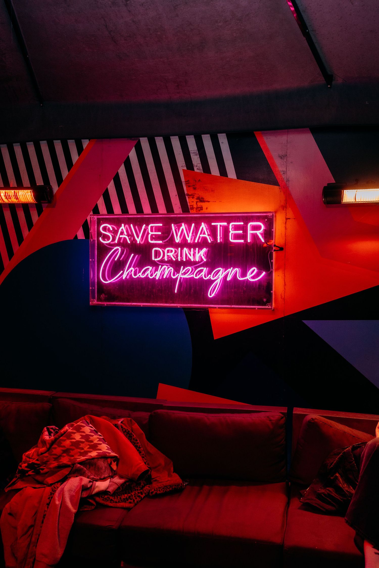 Neon signs in a dark room displaying 'SAVE WATER' and 'DRINK CHAMPAGNE' in glowing pink and blue lights.