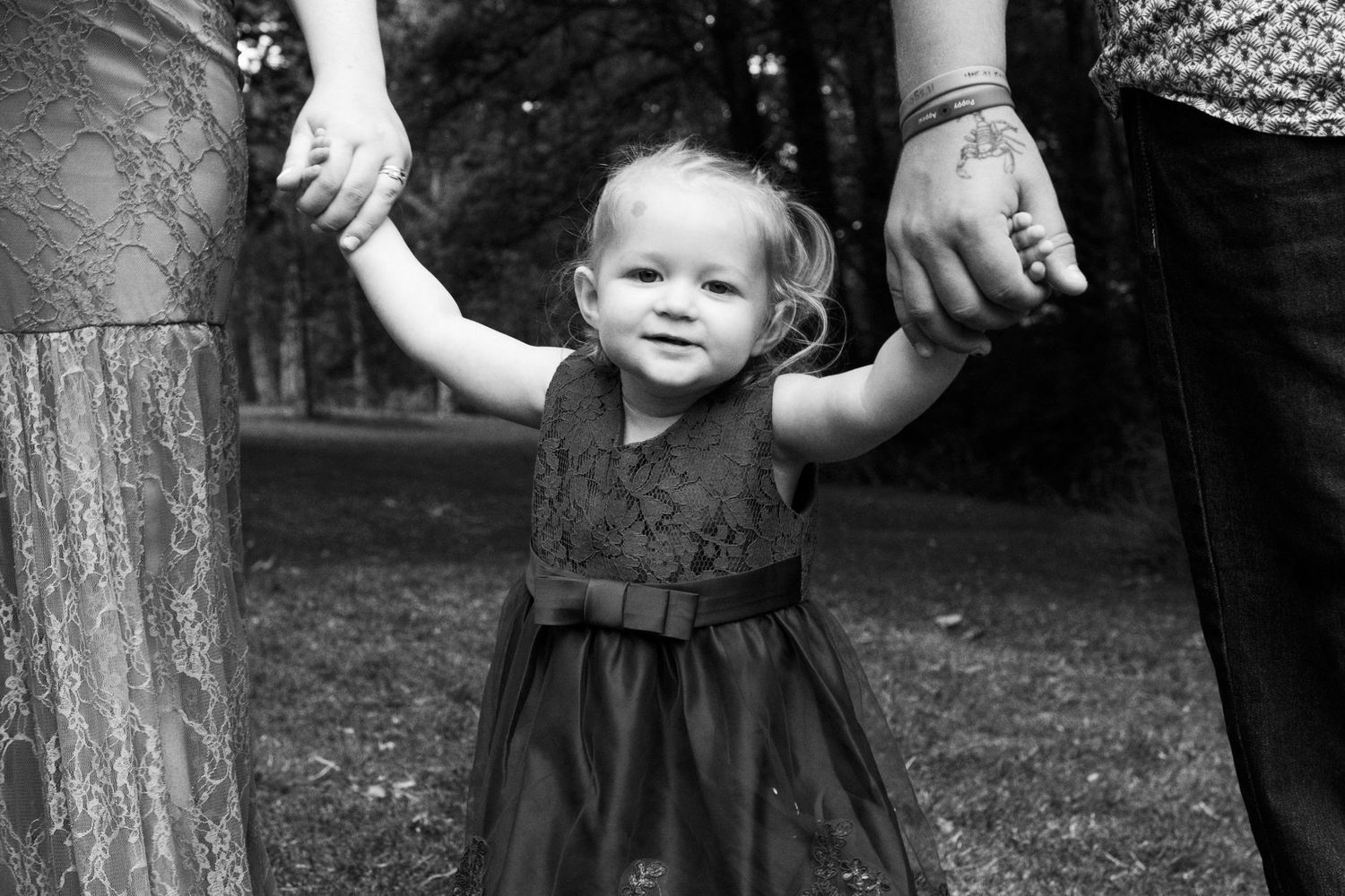 Black and white photo series showing a toddler in a dark dress standing near trees in an outdoor setting.