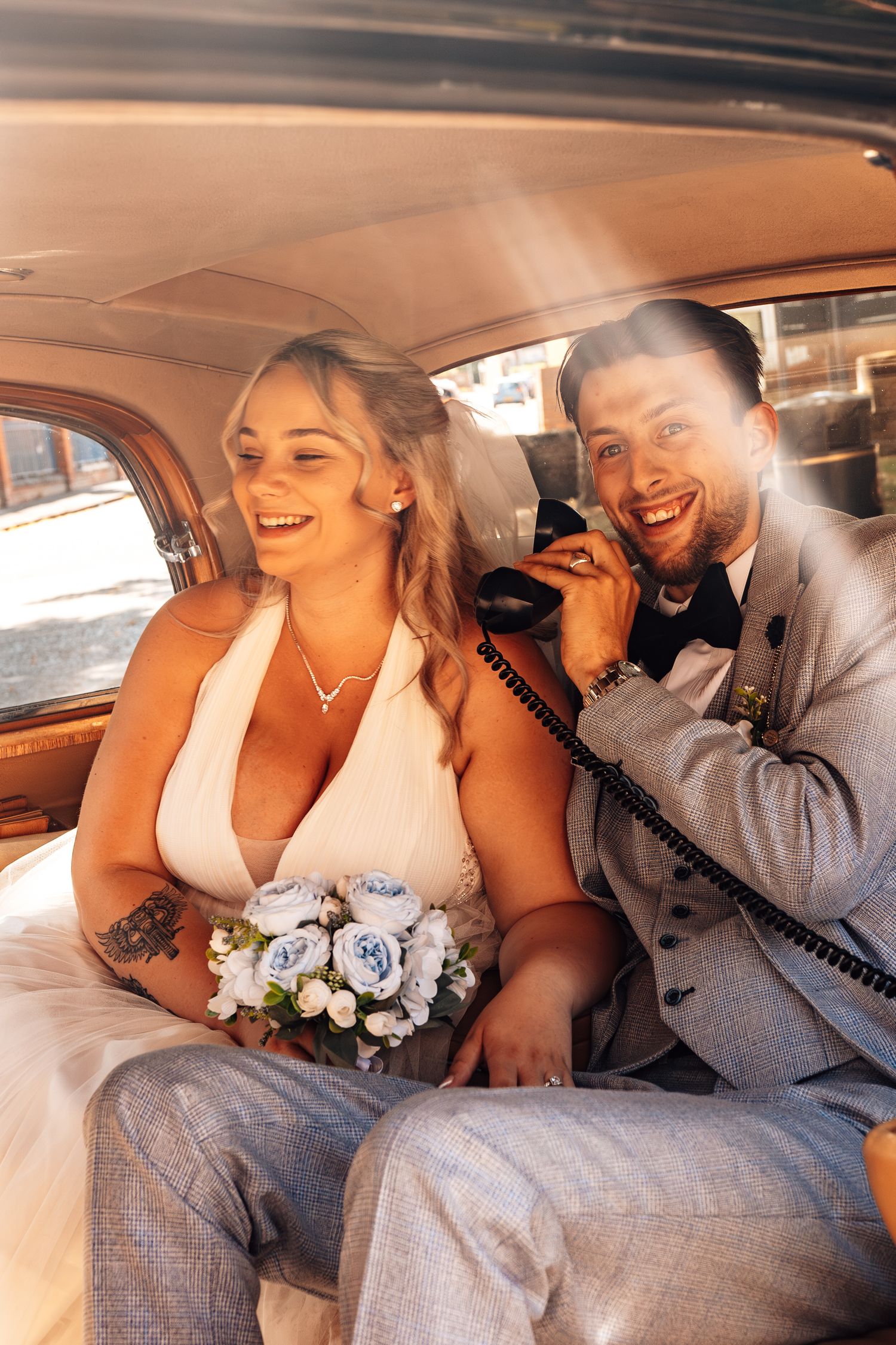 A happy couple shares a joyful moment in the back of a vintage car with a blue and white wedding bouquet.
