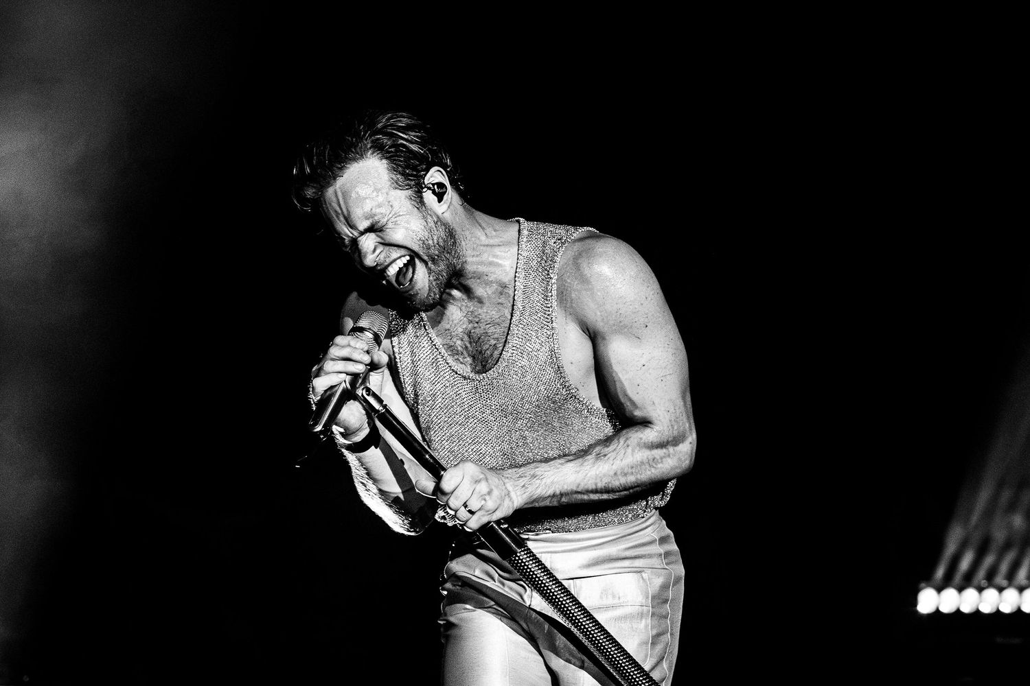 Black and white photograph of a shirtless athlete performing a weightlifting movement in a dramatic lighting setup.