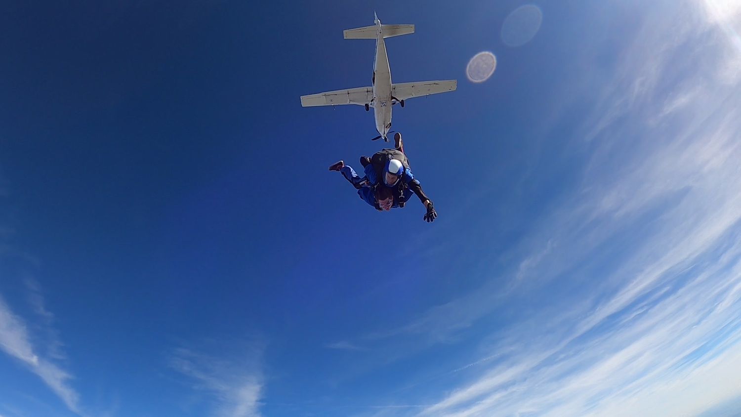 Skydiver glides through bright blue sky with parachute deployed on sunny day.
