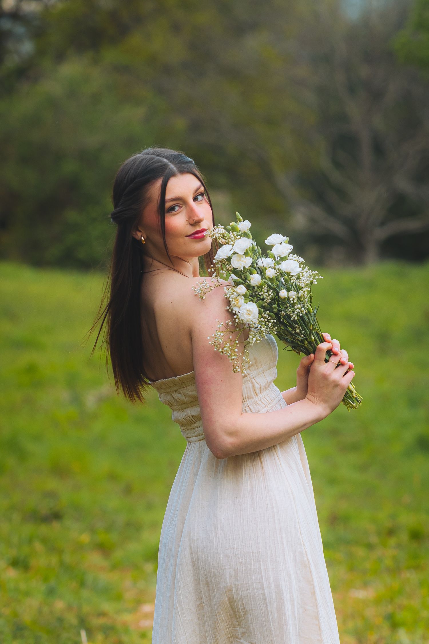 A woman in a flowing white dress poses gracefully in a lush green field with delicate white flowers.