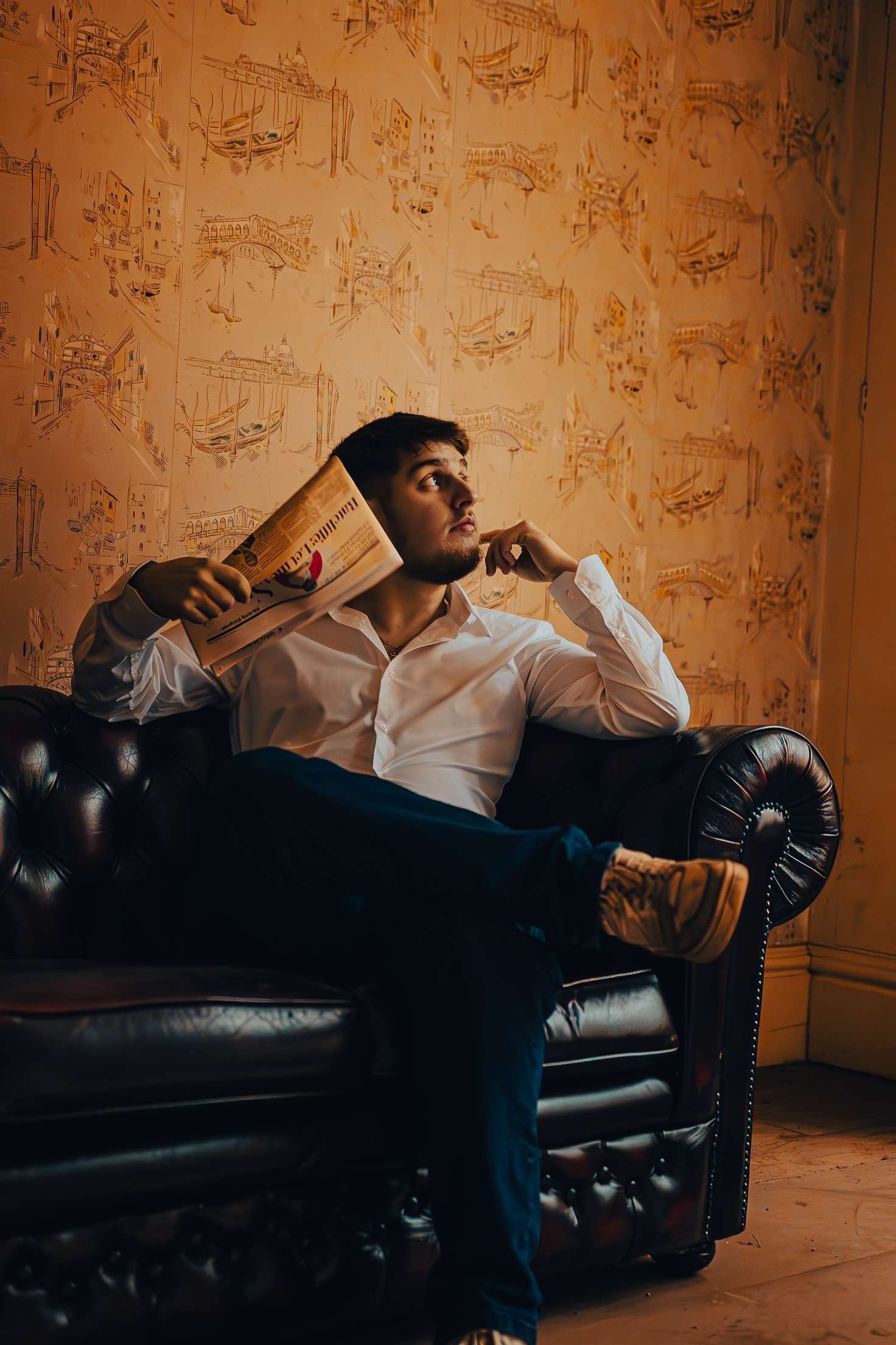 Moody portrait on leather couch with vintage wallpaper background.