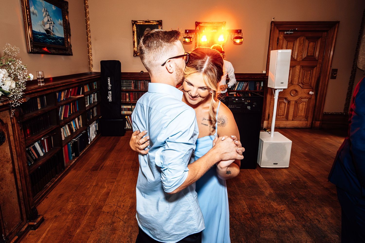 Two dancers move gracefully together during a social dance in a warmly lit room with wooden floors.