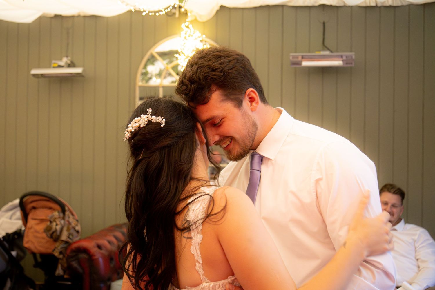 A couple shares an intimate moment during their first dance at a wedding reception with soft lighting and green walls.