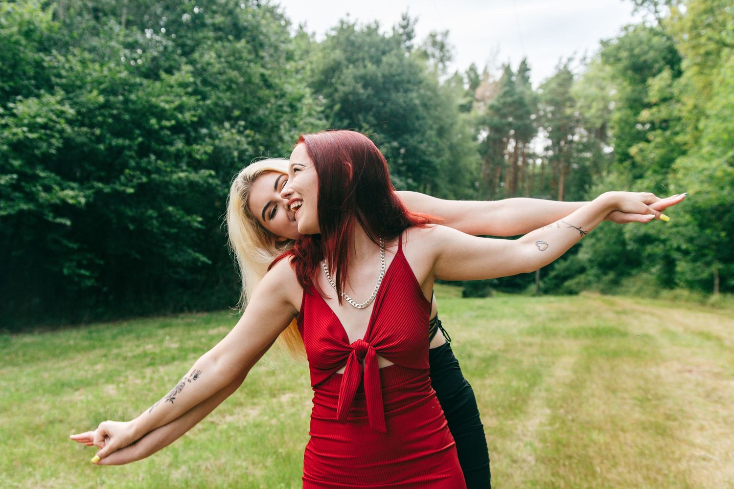 Woman in flowing red dress dances gracefully in a sunlit meadow surrounded by lush green trees.