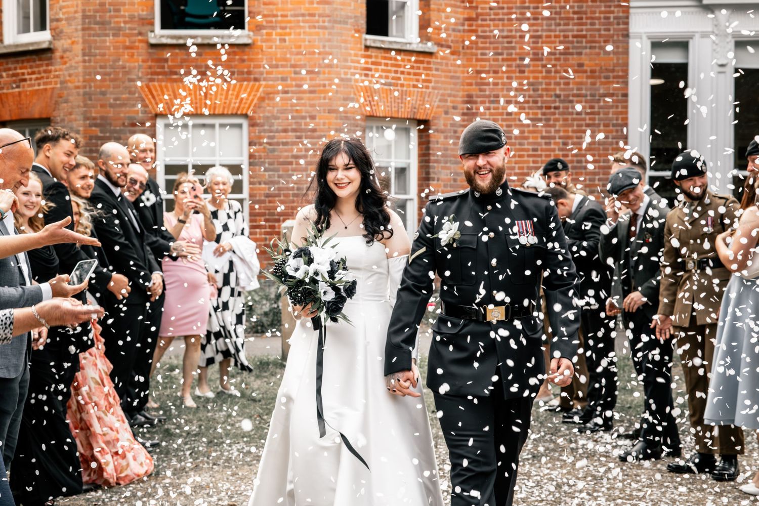 Joyous wedding party celebration with confetti outside historic brick building.