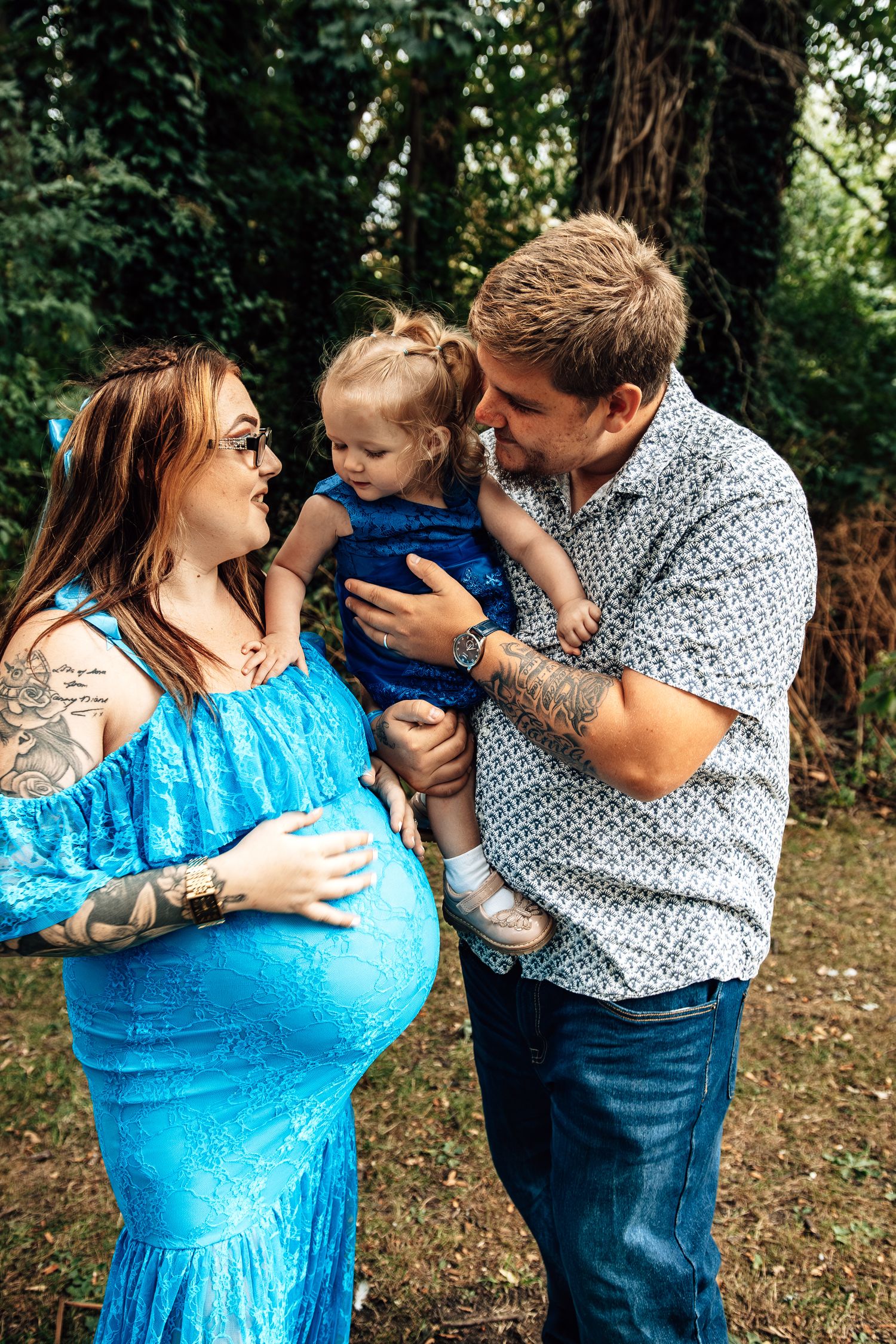 A family shares a playful moment together in a wooded outdoor setting wearing blue and white clothing.