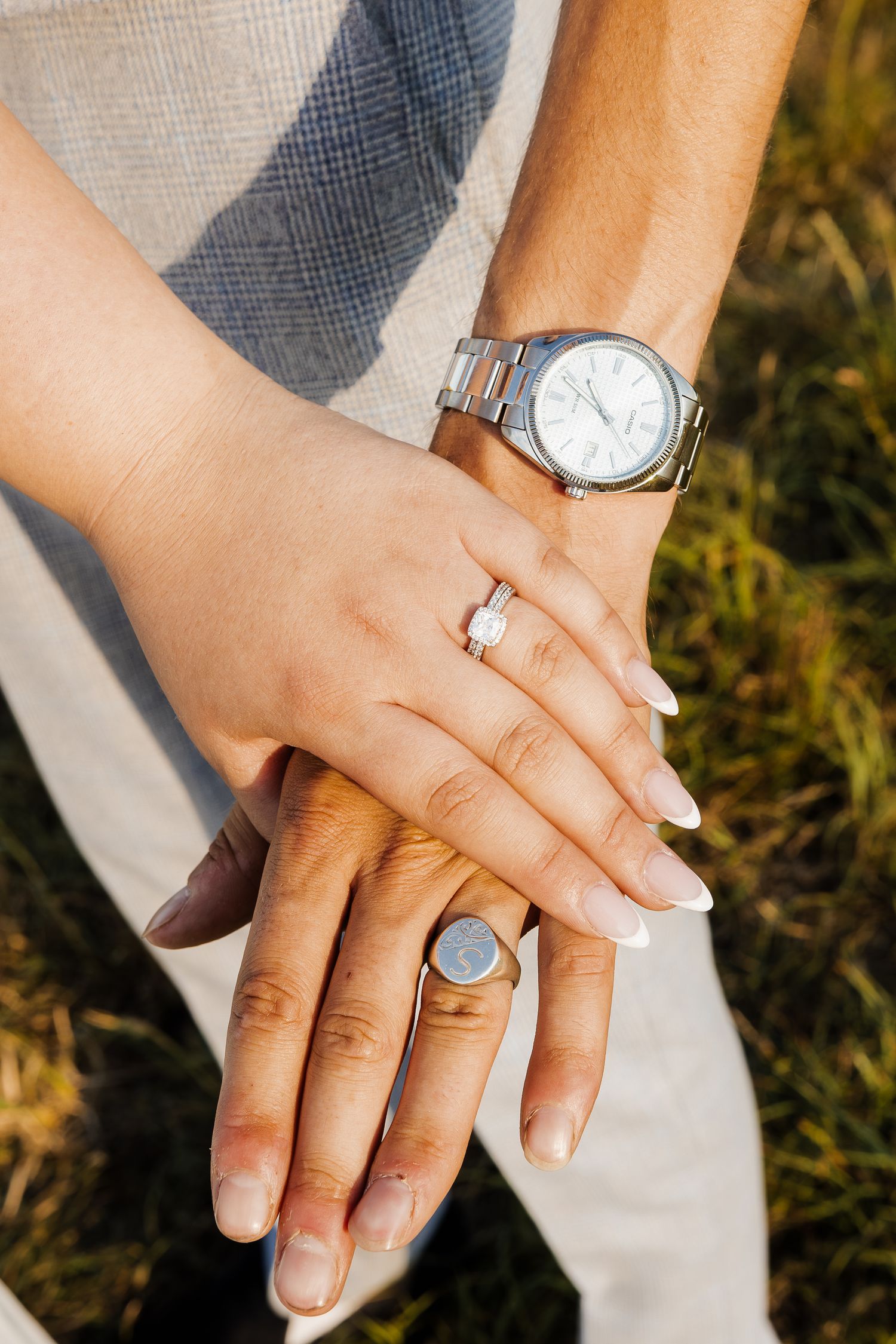 Close-up of hands showing wedding rings and jewelry against natural outdoor lighting.