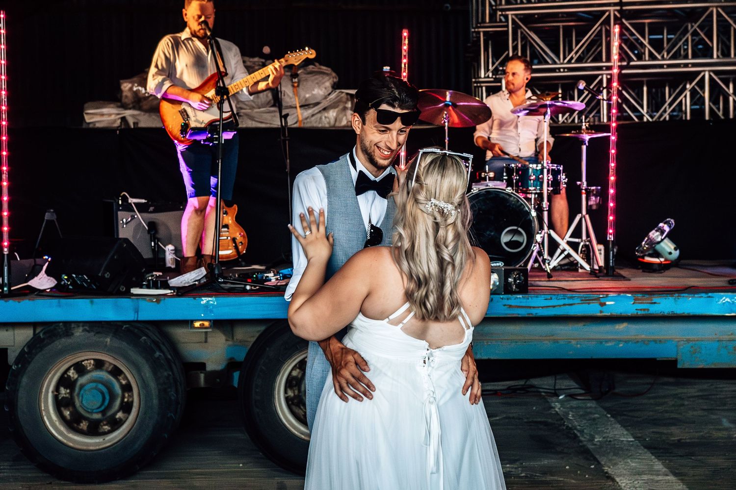 A couple shares their first dance at an outdoor wedding reception while a live band performs on stage behind them.
