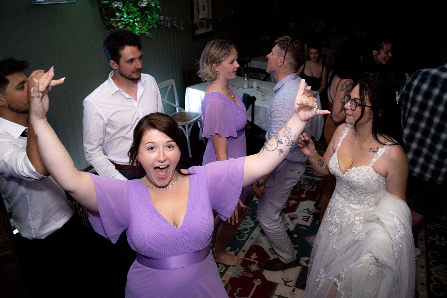 Wedding guests dance and celebrate together on a dimly lit dance floor at an evening reception.