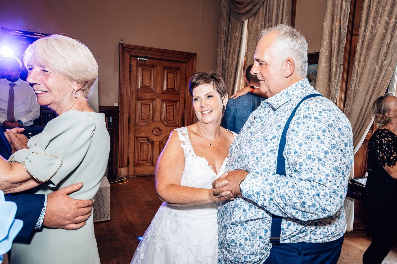 Dancers in formal attire enjoying slow dances at an elegant indoor venue with blue lighting and ornate decor.