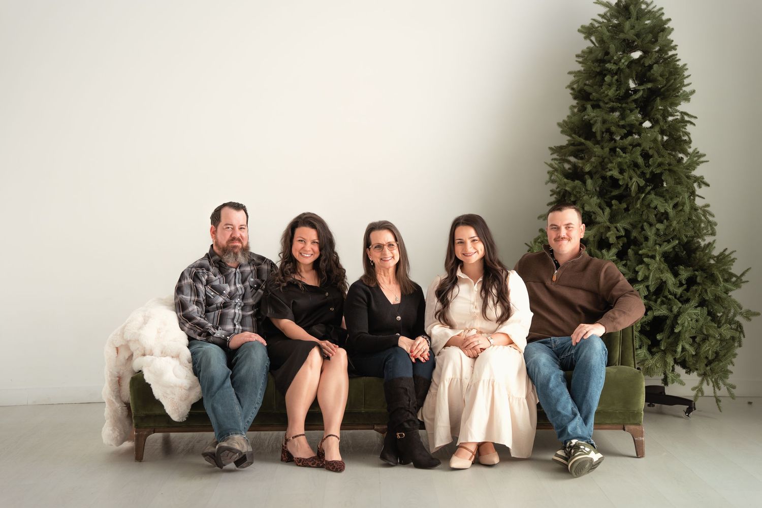 Family of five posing together on a couch near a Christmas tree in a studio.