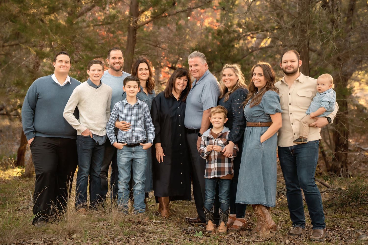 A group of people pose together outdoors in a wooded area during autumn wearing coordinated casual attire.