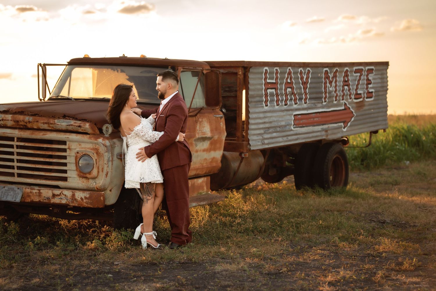 A rustic scene with vintage trucks and farm equipment silhouetted against a warm sunset sky.