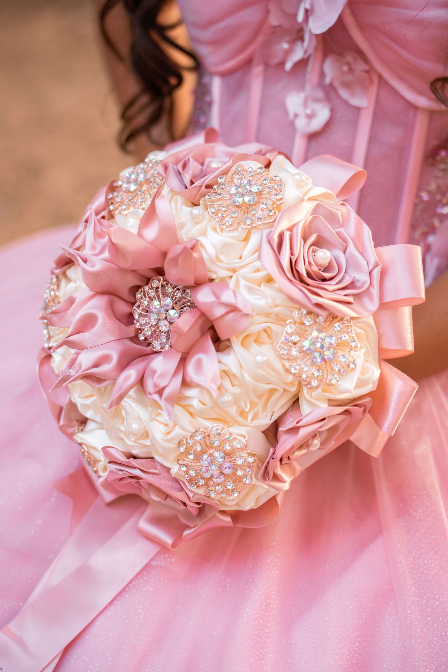 Close-up of elegant pink and cream satin rose bouquet adorned with rhinestone brooches for quinceañera.