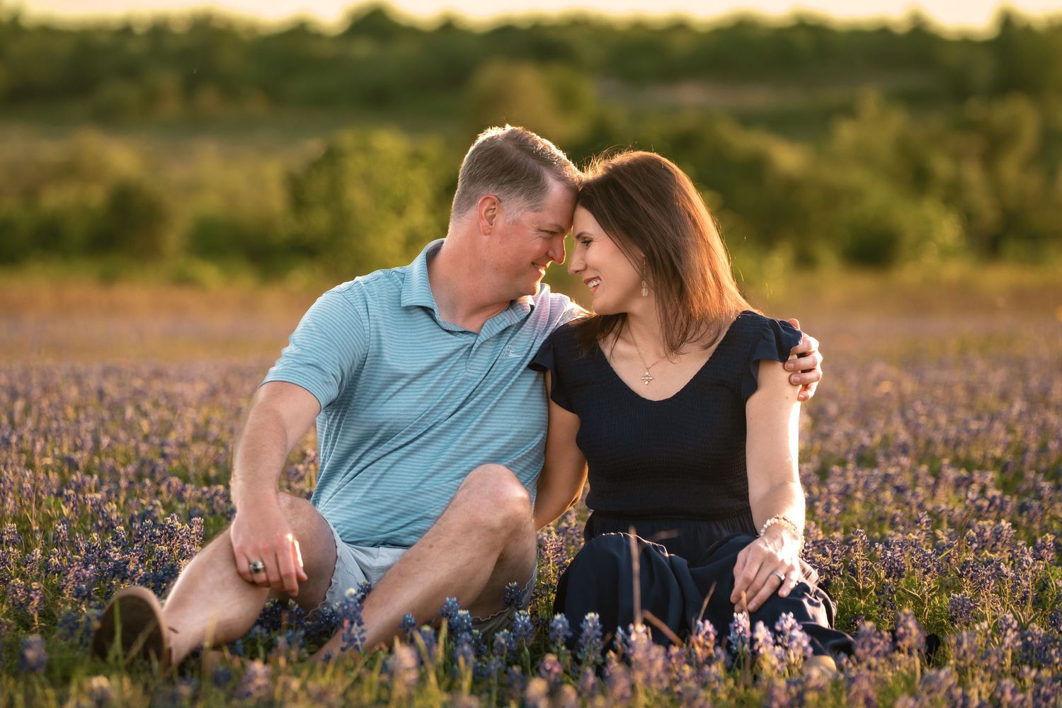 Couple embraces lovingly in a field of vibrant purple wildflowers during golden hour sunset.