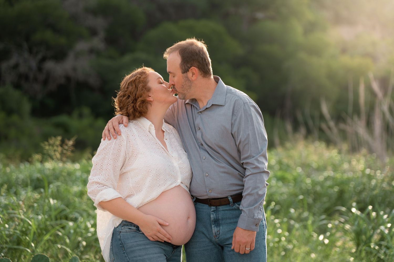 Pregnant couple sharing a tender moment in a sunlit field in Kyle, TX
