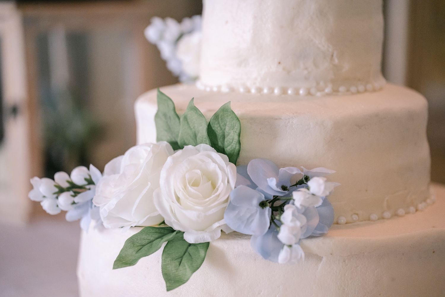 White roses and light blue hydrangea flowers decorate a simple white tiered wedding cake.