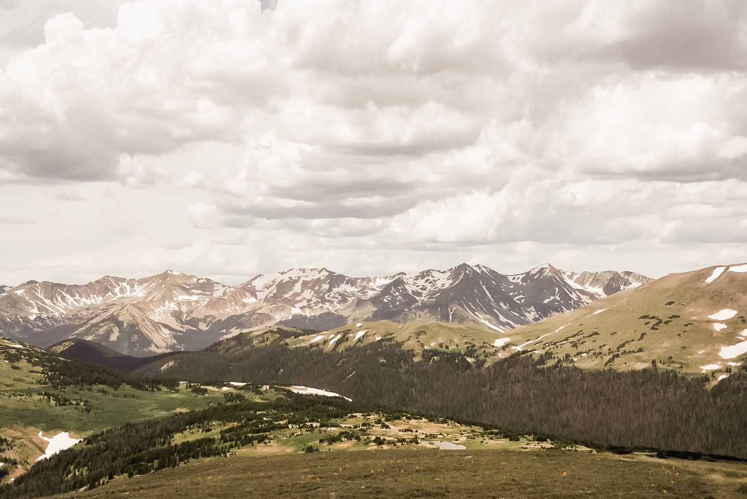 Panoramic mountain landscape with snow-capped peaks and cloudy skies stretching across the horizon.
