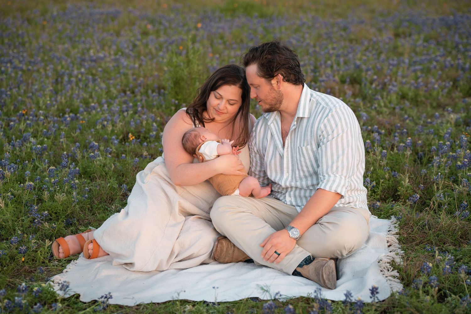 Couple nestled together on white blanket in beautiful field of blooming purple wildflowers during golden hour.