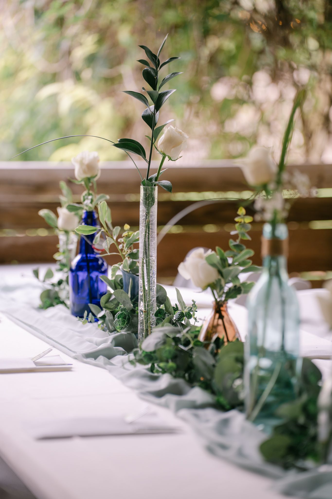 Elegant wedding table decor with blue glass vases and delicate candlesticks arranged alongside eucalyptus greenery and white linens.