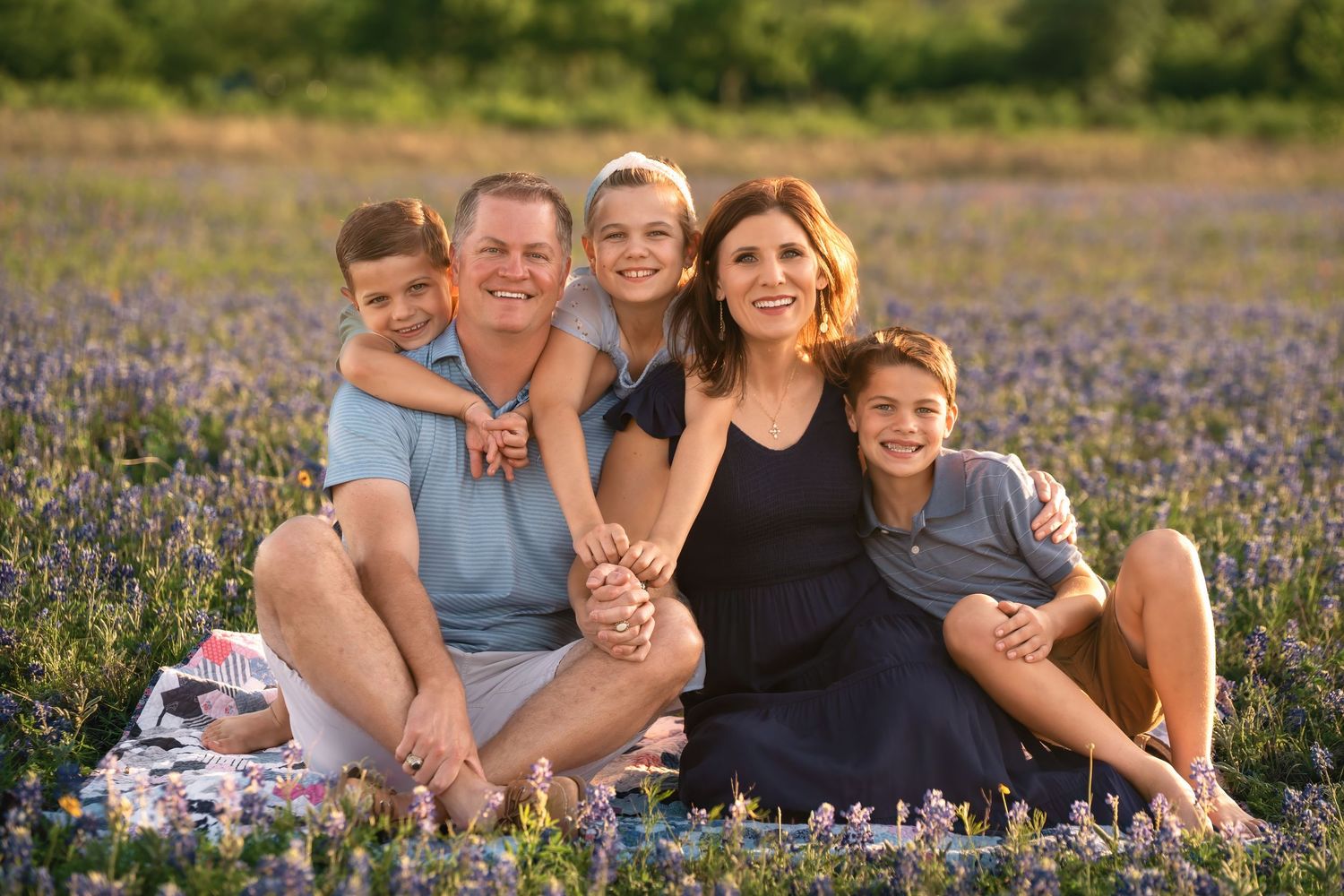 A group sits together in a blooming field of purple wildflowers on a sunny afternoon.