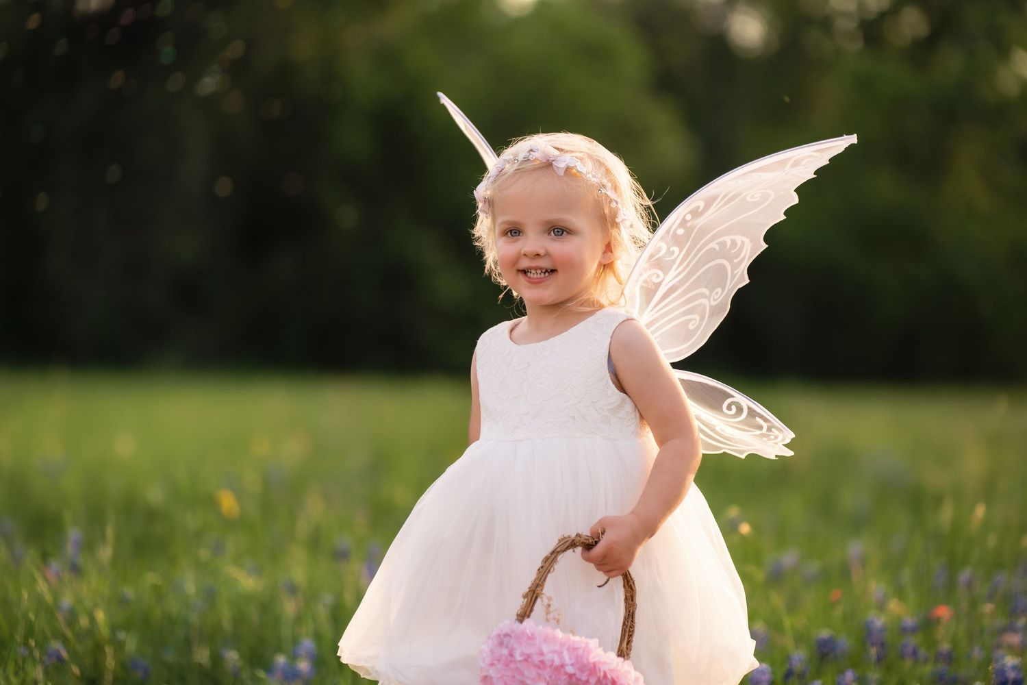 A young child in a white dress holds a lace parasol while standing in a field of wildflowers on a sunny day.