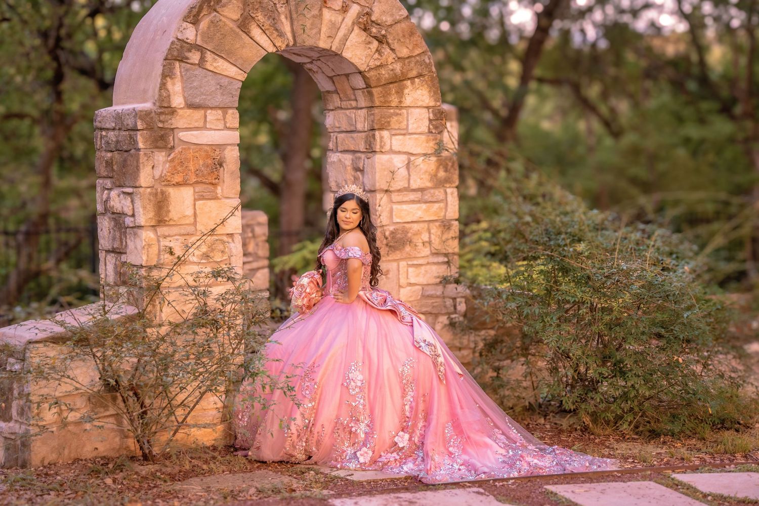 Pink tulle dress flowing elegantly against stone archway and natural backdrop.
