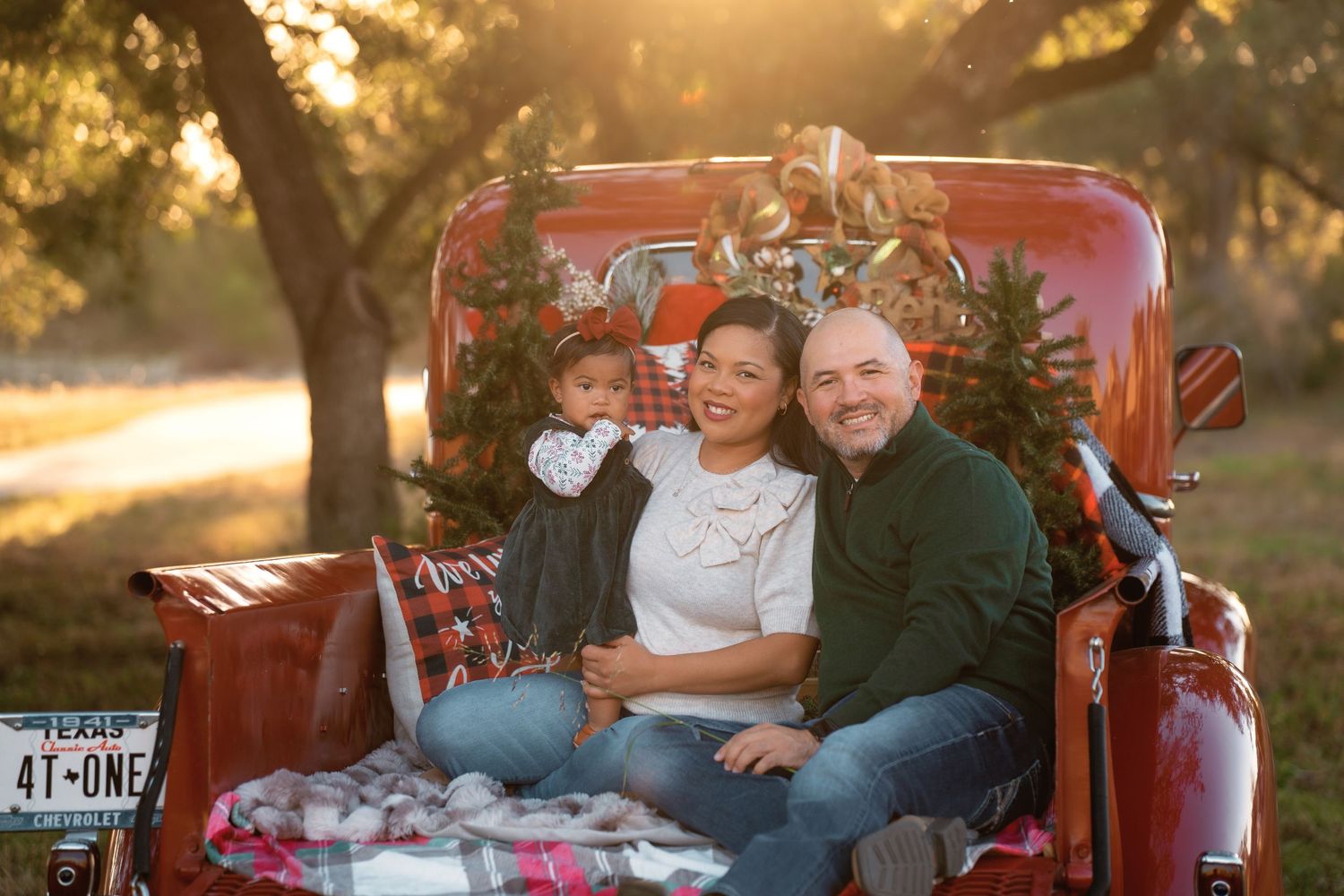 Family posing in red vintage truck bed with Christmas decorations at golden hour in Texas.