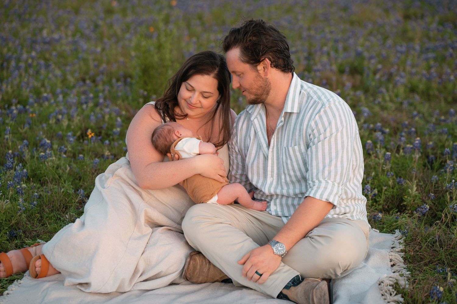 A couple sits lovingly in a blooming field of purple wildflowers on a sunny day.