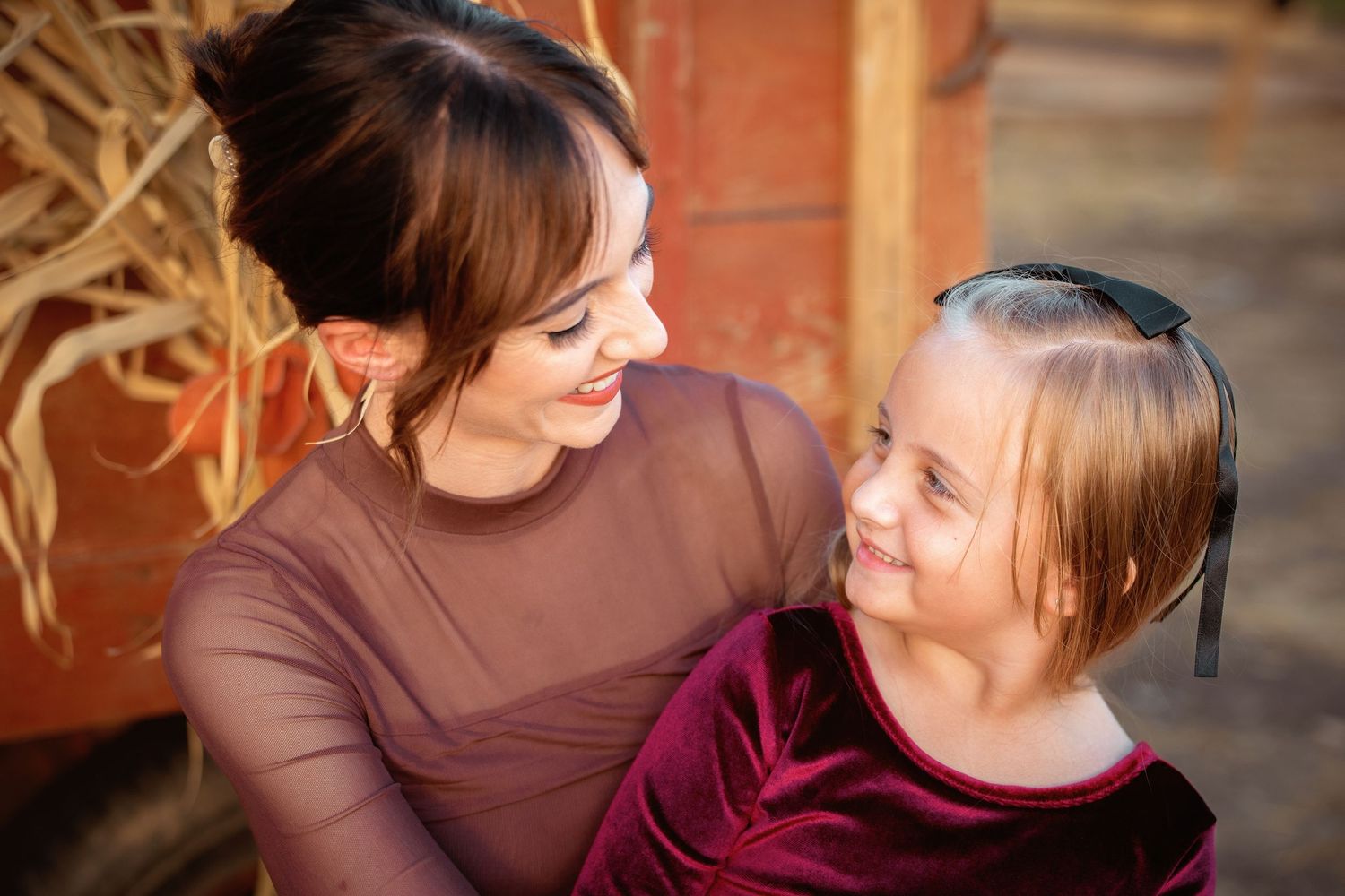 A woman and a young girl with Down syndrome share a warm smile outdoors in autumn.