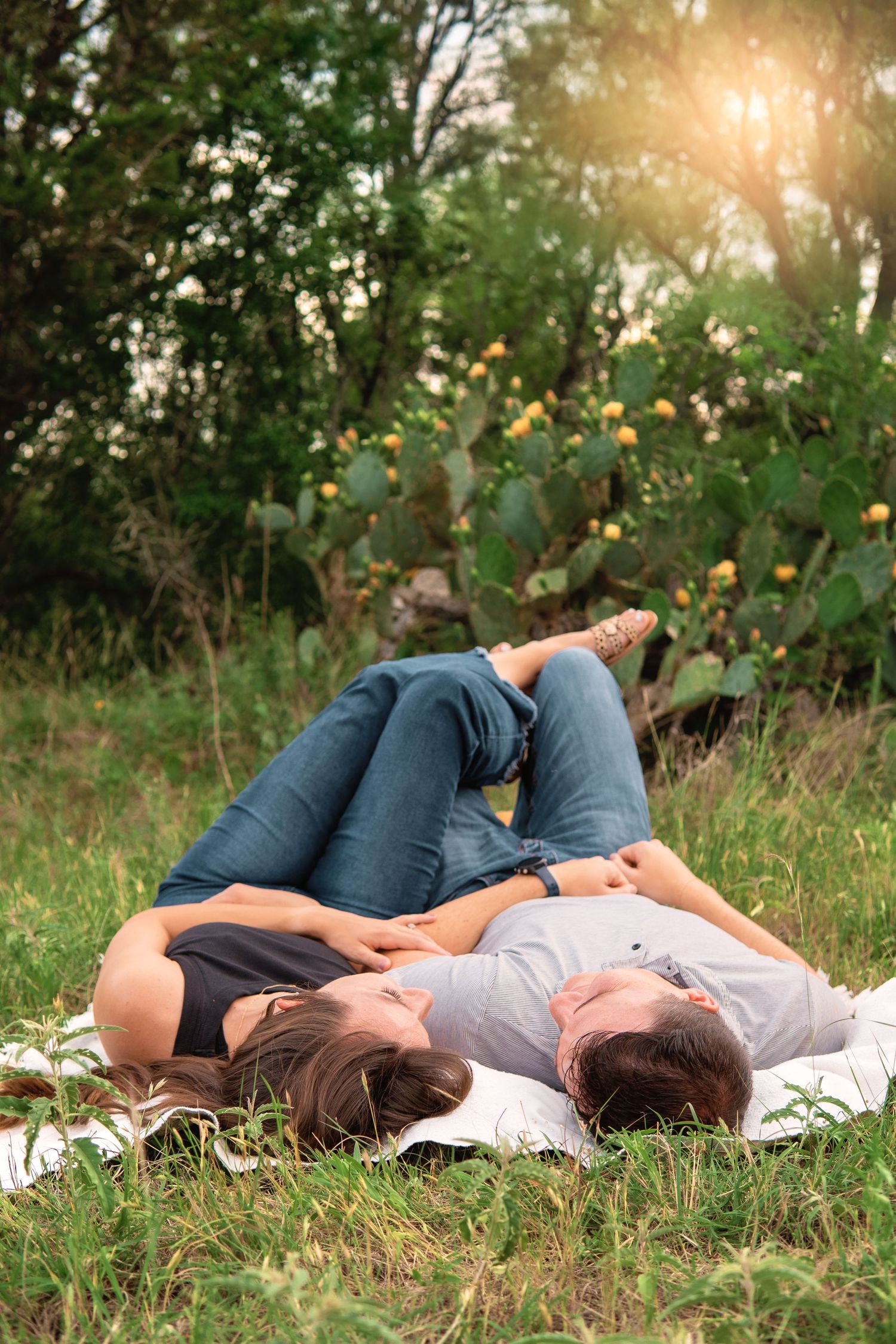 Couple lying on a blanket in a lush green park, relaxing together on a sunny day.