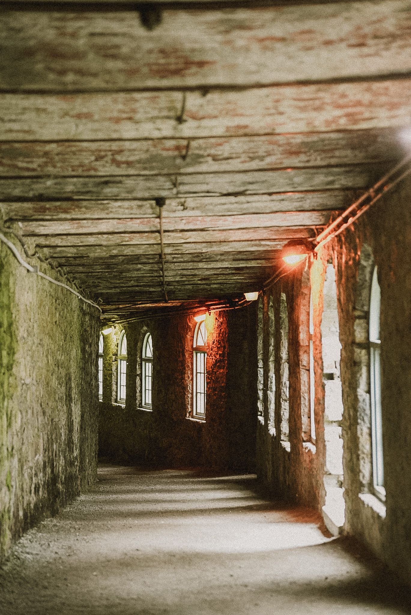 Dark and atmospheric hallway in an abandoned building with natural light streaming through windows.