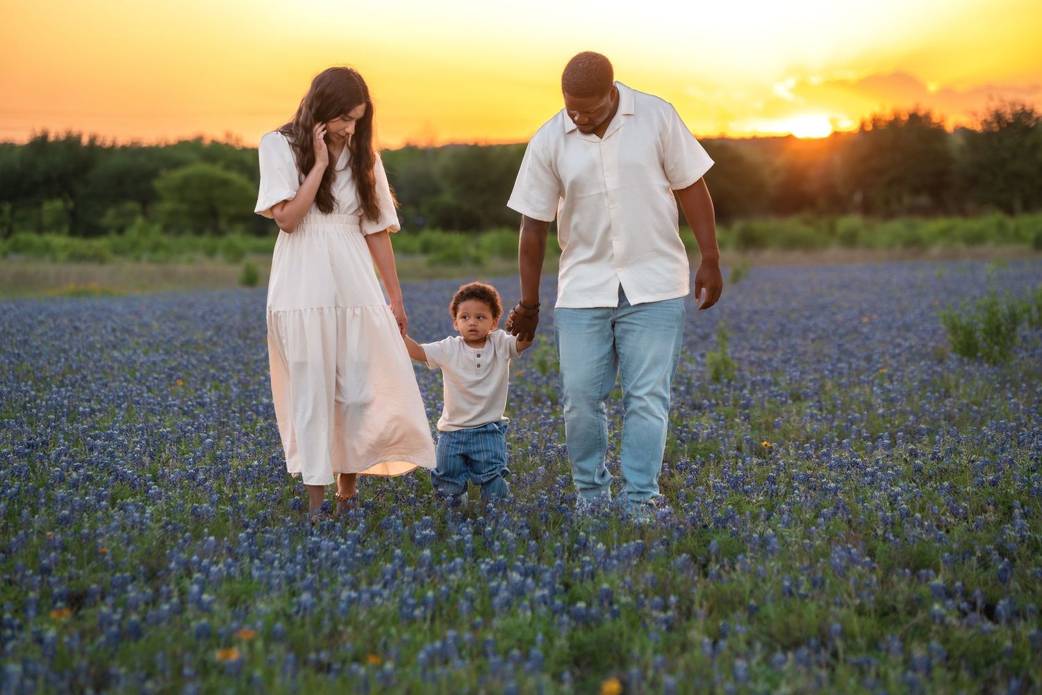 Family walking together through a blooming bluebonnet field at sunset in Texas.