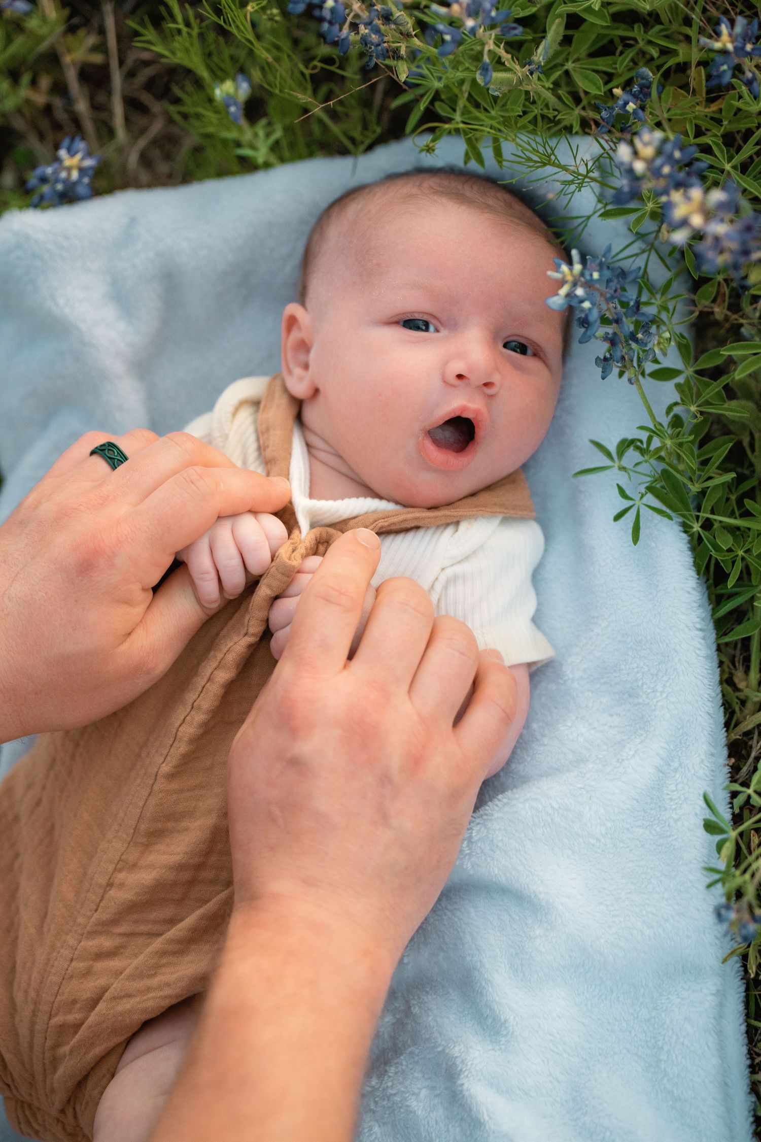 A sequence of photos showing a baby getting their nose cleaned with a nasal aspirator while lying on a blue blanket outdoors.